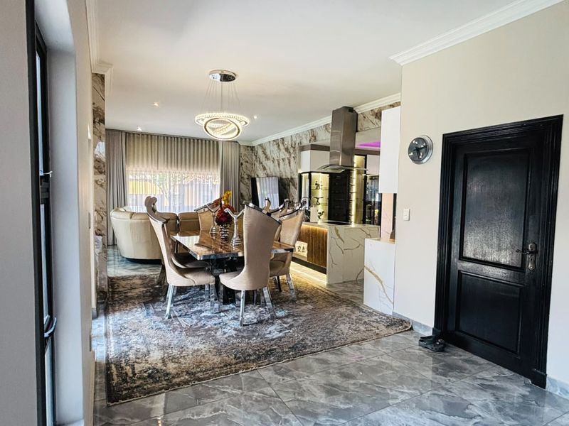 An elegant open-plan living and dining area featuring marble-effect wall cladding, polished floor tiles, and a modern kitchen with integrated cabinetry and lighting.