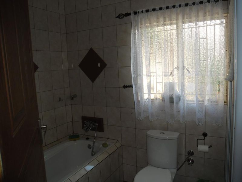 A functional bathroom featuring a built-in bathtub, toilet, and tiled wall finishes with security bars on the window.
