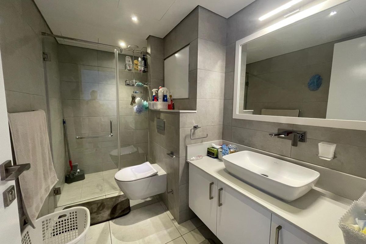 Modern bathroom featuring a wall-mounted toilet, glass-enclosed shower, and a sleek vanity with a vessel sink and large mirror.