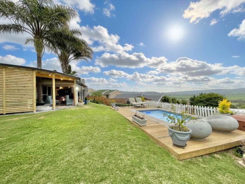 Outdoor pool area featuring timber decking, a picket fence, and a covered patio overlooking the surrounding landscape.