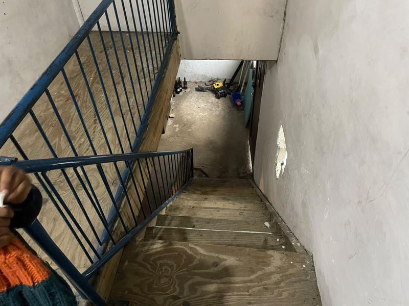A view looking down a staircase with metal railings, showing significant wear to the wall finishes and stair treads.