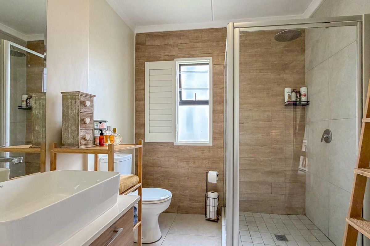 Modern bathroom featuring a glass-enclosed shower, wood-look tiled accent wall, vessel sink vanity, and white toilet with plantation-style window shutters.