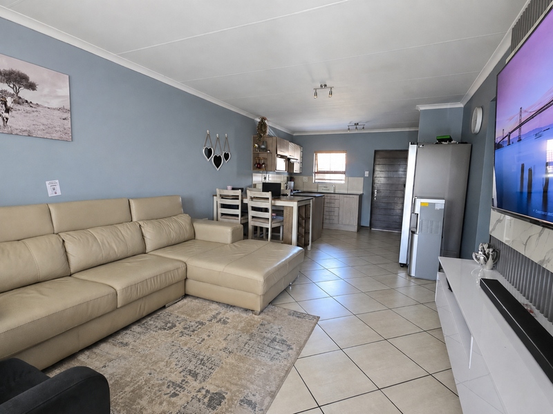 An open-plan living and kitchen area featuring tiled flooring, neutral wall tones, and a functional kitchen layout with built-in cabinetry and an island.