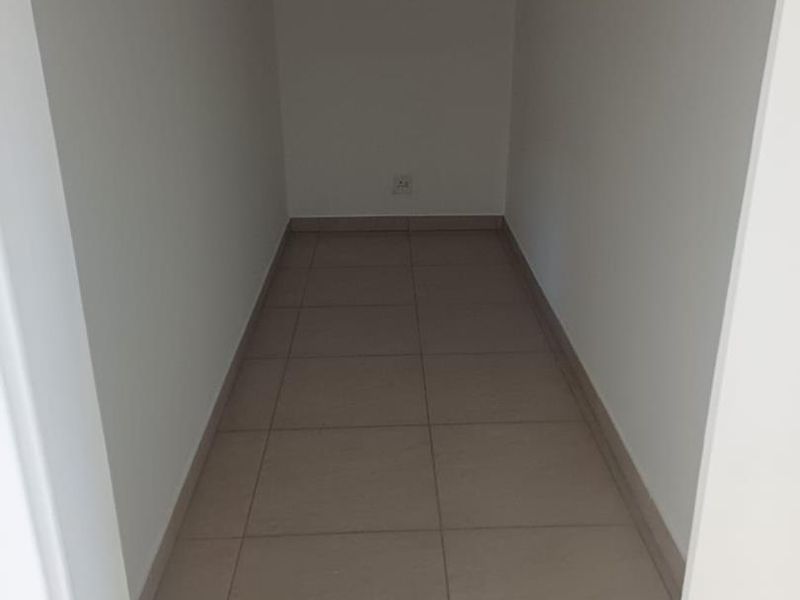 A compact, empty office space featuring neutral tiled flooring and a wall-mounted air conditioning unit.