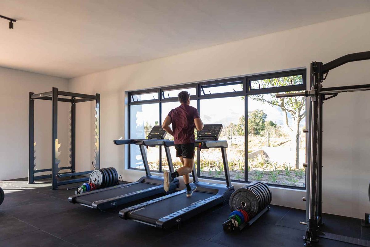 A modern, well-lit home gym featuring large windows with garden views and durable tiled flooring, equipped for a comprehensive workout experience.