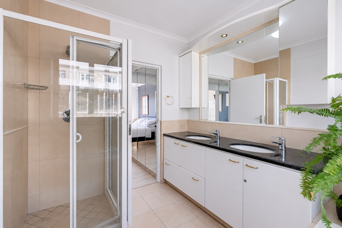 Modern bathroom featuring a double vanity with granite countertops, built-in cabinetry, a large wall mirror, and a separate glass-enclosed shower.