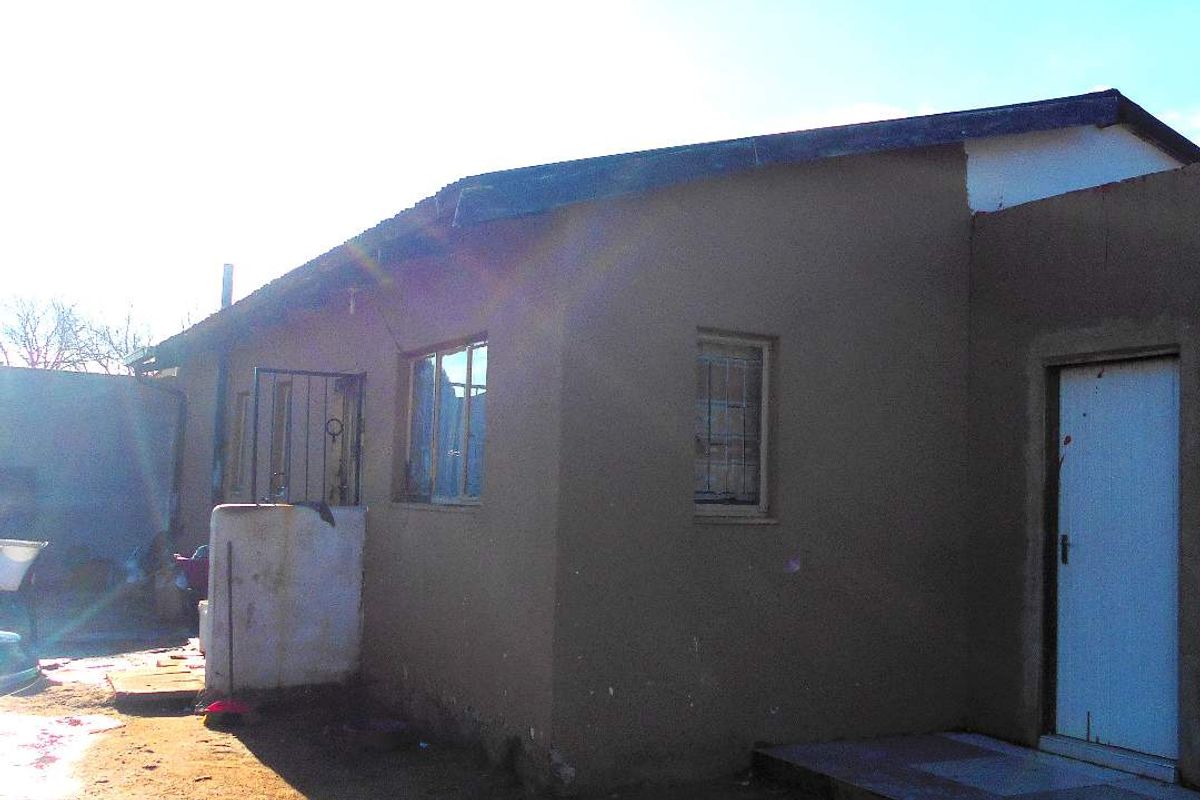 Rear exterior view of the property showing a simple facade with a concrete step and security gate access.