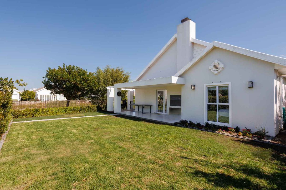 Rear view of the property featuring a well-maintained lawn, a covered patio area with a built-in braai, and a prominent chimney.
