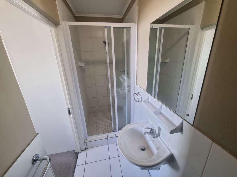 A functional bathroom featuring a shower enclosure, wall-mounted basin, and tiled finishes, offering a clean and practical space.
