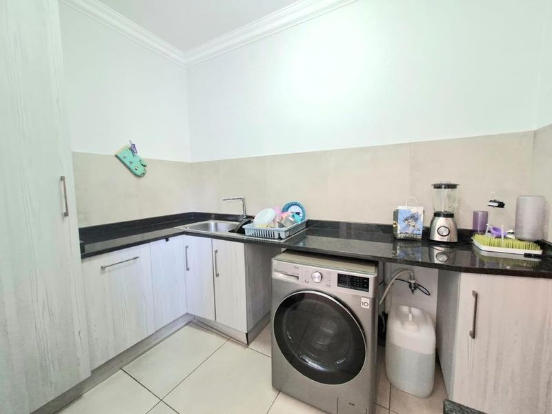 A functional laundry area featuring granite countertops, built-in cabinetry, a stainless steel sink, and tiled finishes.