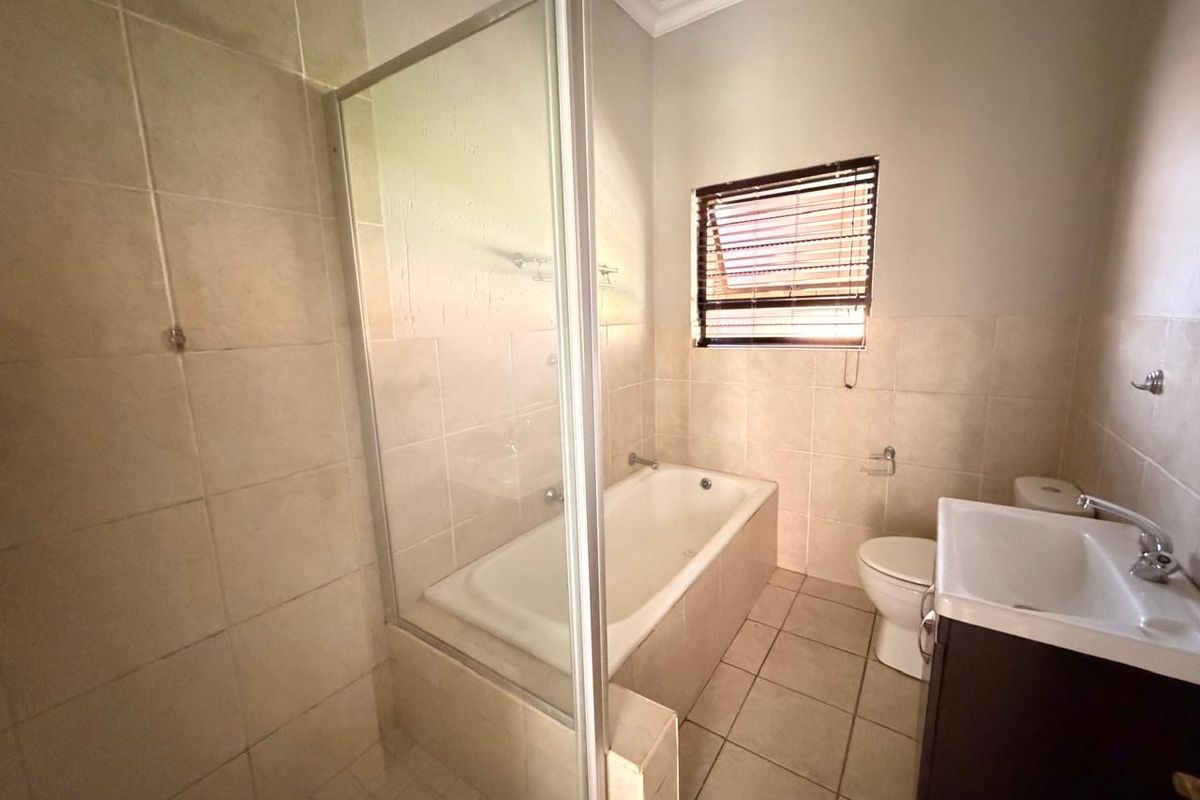 A functional bathroom featuring a built-in bathtub, a separate glass-enclosed shower, a vanity basin, and a toilet with neutral wall and floor tiling.
