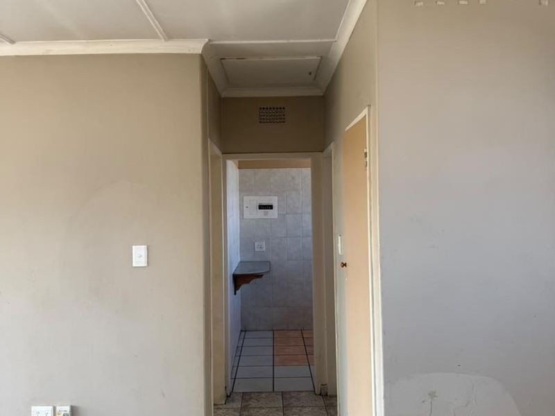 A vacant hallway featuring tiled flooring and neutral wall finishes, leading to an adjacent utility or kitchen area with a built-in shelf.
