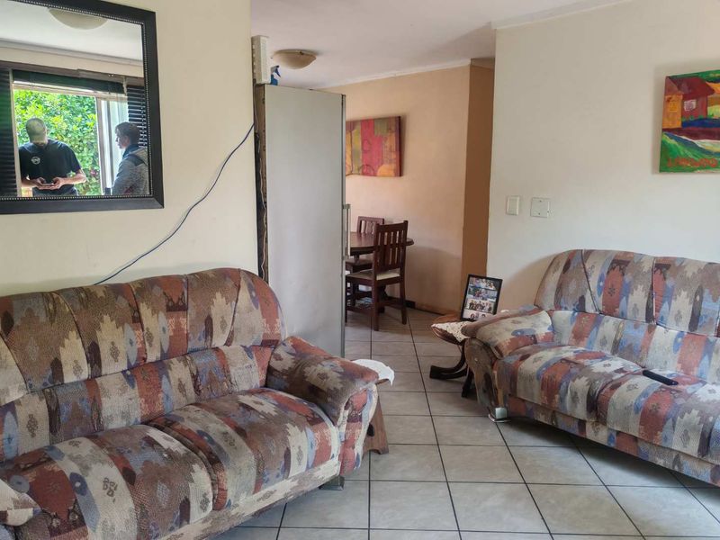 A living room area featuring ceramic floor tiles and a sliding window, currently showing signs of wear and requiring cosmetic updates.