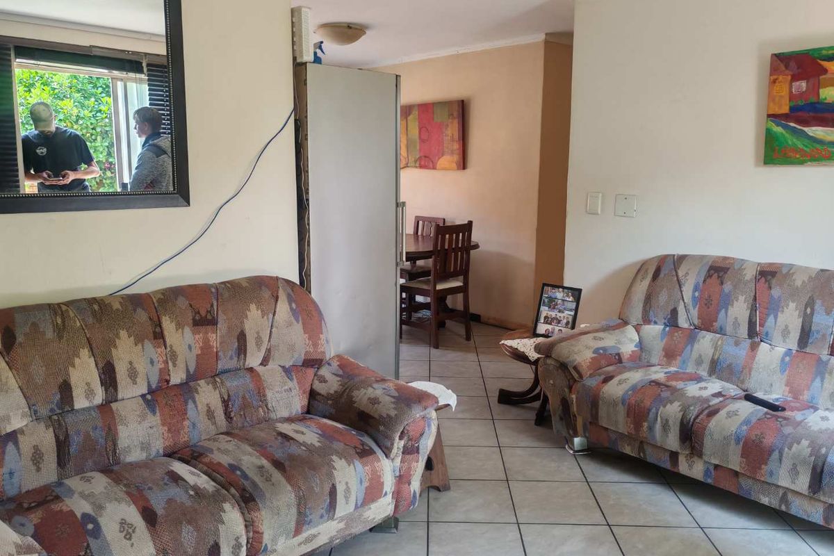 A living room area featuring ceramic floor tiles and a sliding window, currently showing signs of wear and requiring cosmetic updates.