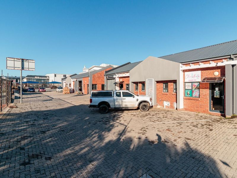 Front exterior view of a commercial property complex featuring brick facades, paved parking area, and secure perimeter fencing.
