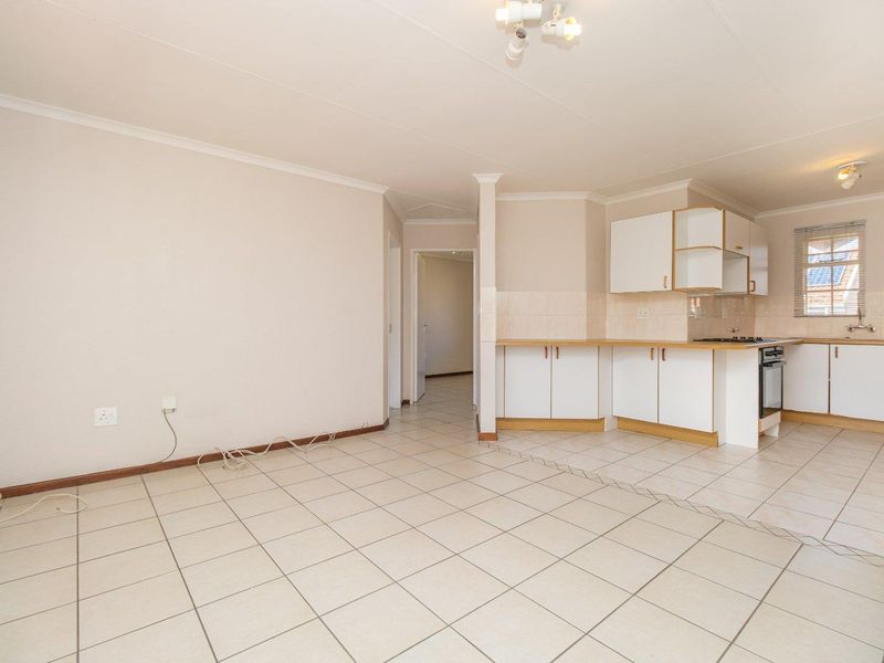 An open-plan living and kitchen area featuring tiled flooring, white built-in cabinetry, and a functional kitchen layout with a built-in oven and hob.