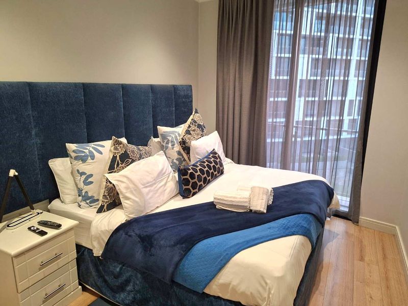 A well-maintained bedroom featuring laminate flooring and a large floor-to-ceiling window with integrated curtain tracks, offering a clean and modern aesthetic.