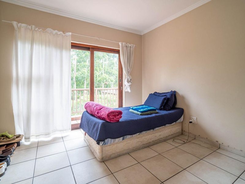 A bedroom featuring tiled flooring, neutral walls, and a sliding glass door providing access to an outdoor balcony area.