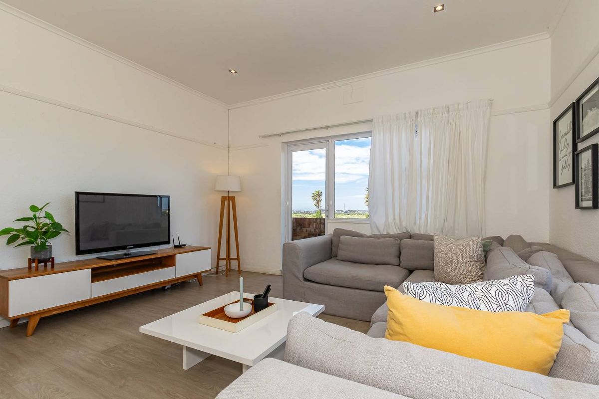 A bright and airy living room featuring wood-look flooring, recessed ceiling lighting, and a glass door providing access to an outdoor balcony area.