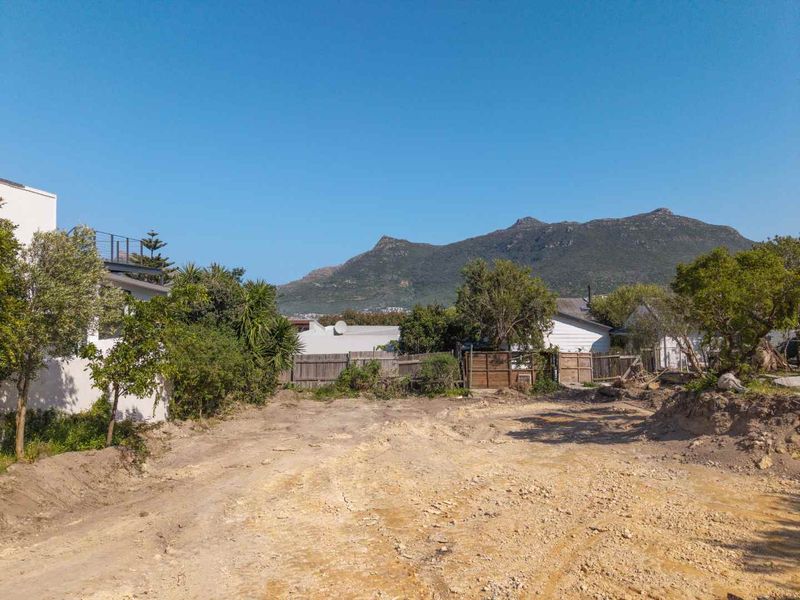 A vacant residential plot featuring natural soil terrain, perimeter timber fencing, and scenic mountain views, offering a blank canvas for development.