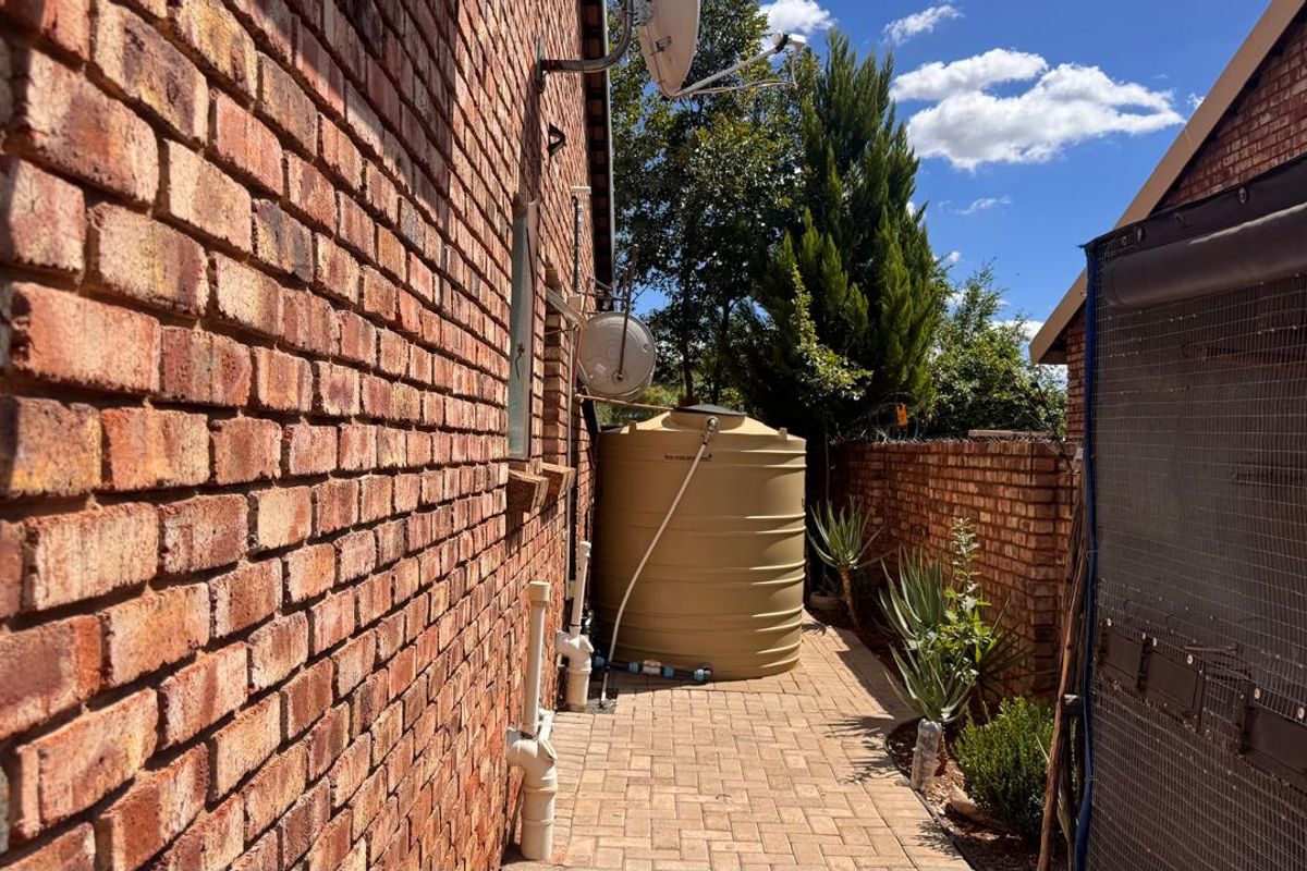 Side exterior area featuring a brick townhouse facade, paved walkway, and a large plastic water storage tank.