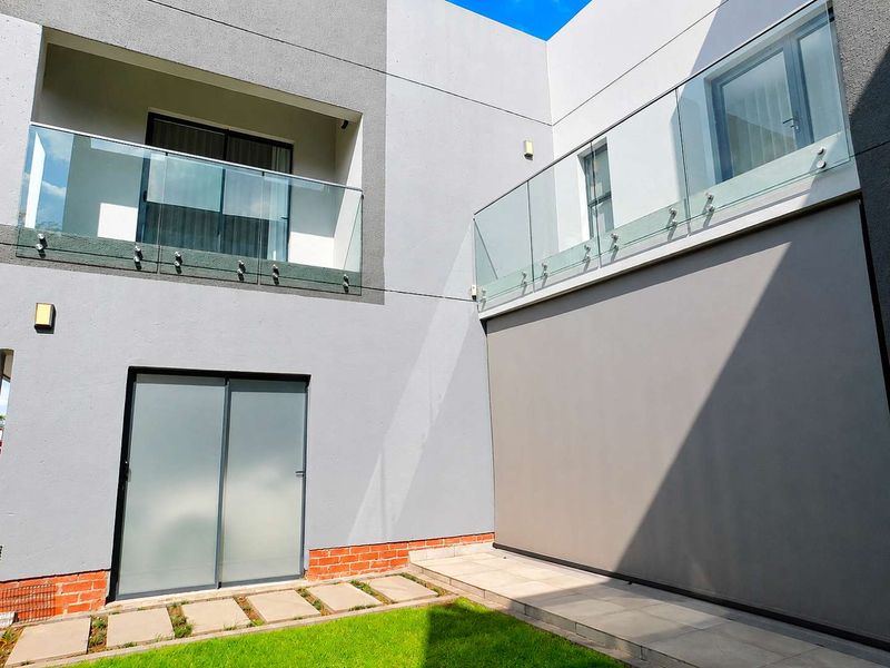 Modern rear exterior view featuring glass balustrades, sliding doors, and a well-maintained paved garden area.