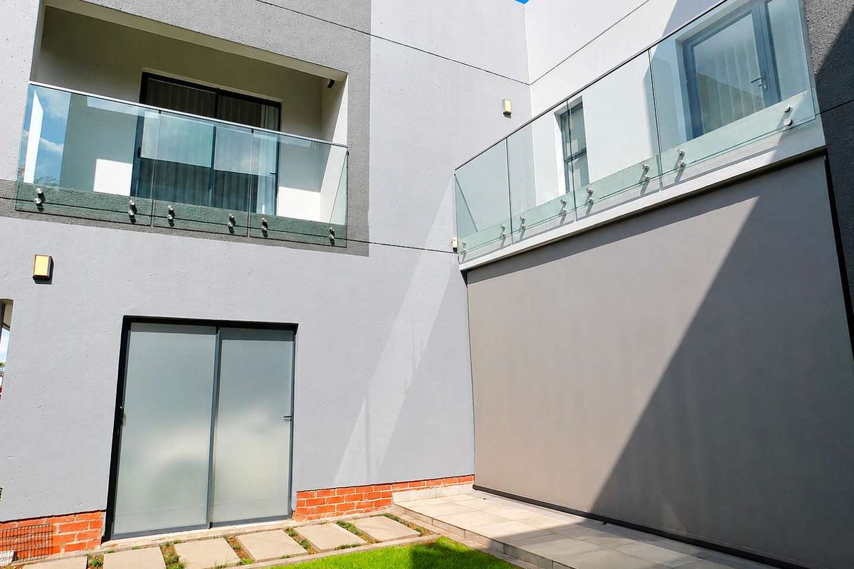 Modern rear exterior view featuring glass balustrades, sliding doors, and a well-maintained paved garden area.
