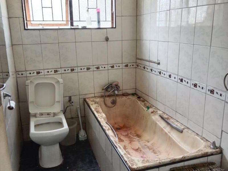 A dated bathroom featuring a built-in bathtub, toilet, and tiled finishes, requiring significant renovation and deep cleaning to restore functionality and aesthetic appeal.