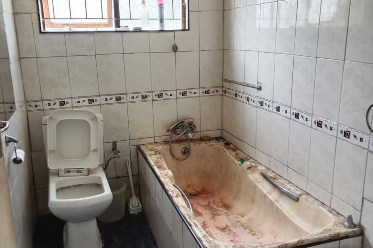 A dated bathroom featuring a built-in bathtub, toilet, and tiled finishes, requiring significant renovation and deep cleaning to restore functionality and aesthetic appeal.