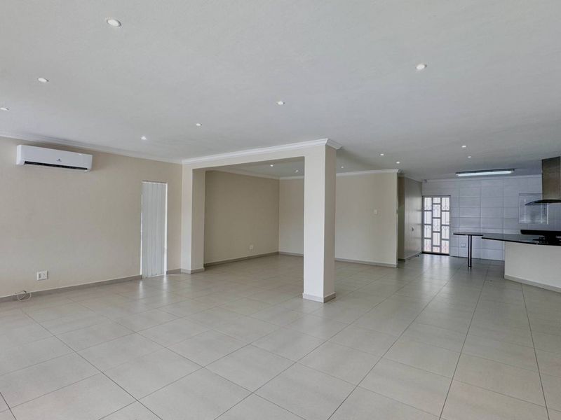 Spacious open-plan living area featuring neutral tiled flooring, recessed lighting, an air conditioning unit, and a modern kitchen with a breakfast island.