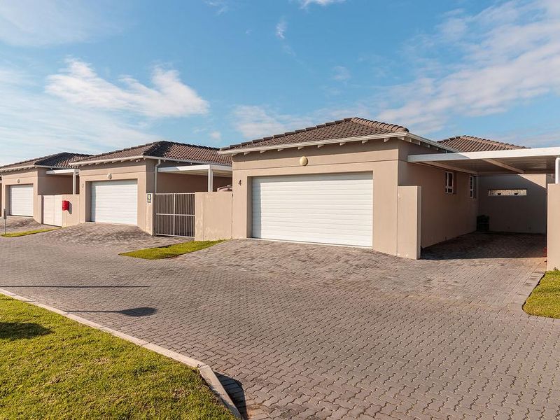 Front view of a modern townhouse complex featuring paved driveways, sectional garage doors, and integrated carports under a tiled roof structure.