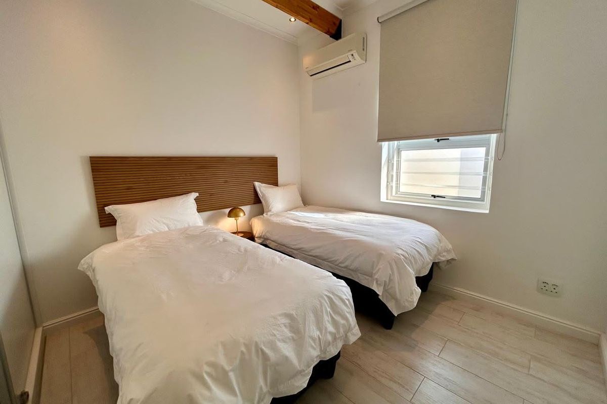 A well-maintained bedroom featuring tiled flooring, an exposed timber ceiling beam, a split-system air conditioner, and a modern timber slat headboard.