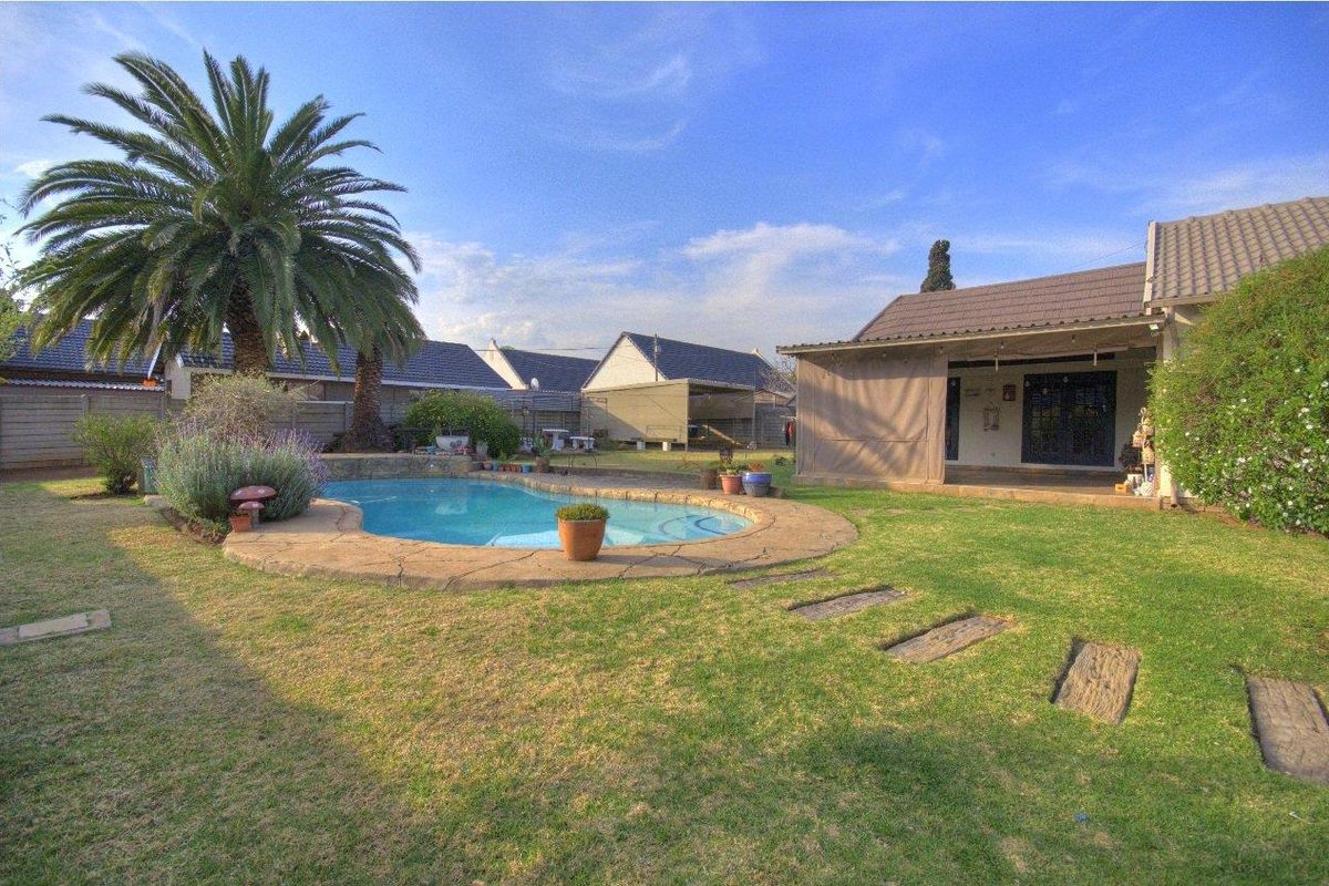 Rear garden view featuring a swimming pool with paved surround, a covered patio area, and established landscaping.