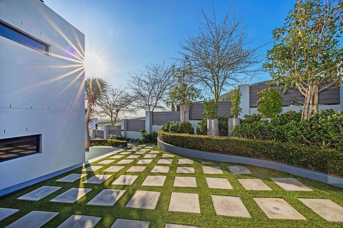 A modern, landscaped rear garden featuring a geometric paved walkway, manicured hedges, and contemporary boundary fencing against a clear sky.