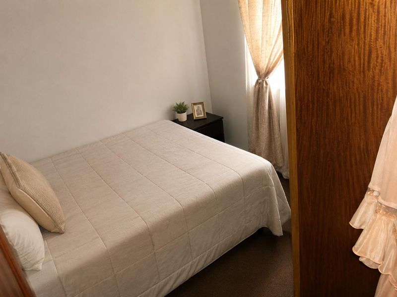 A compact bedroom featuring carpeted flooring and a window with installed curtain rods, providing a functional and private sleeping space.