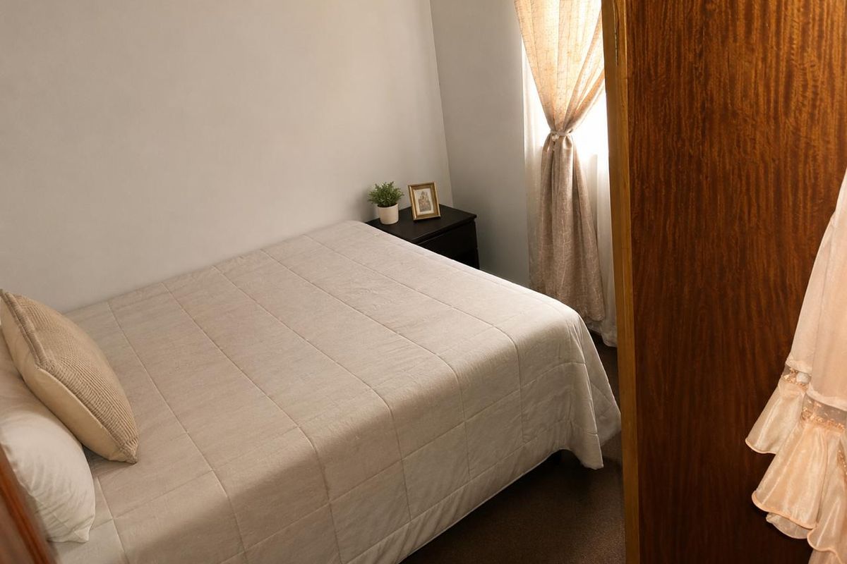 A compact bedroom featuring carpeted flooring and a window with installed curtain rods, providing a functional and private sleeping space.