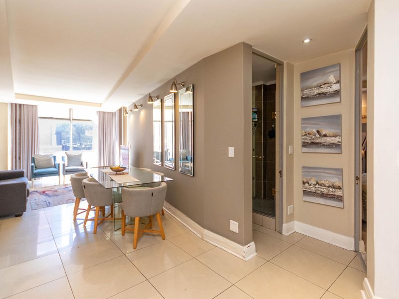 An open-plan living and dining area featuring neutral tiled flooring, recessed lighting, and a seamless transition to the adjacent bathroom and bedroom spaces.