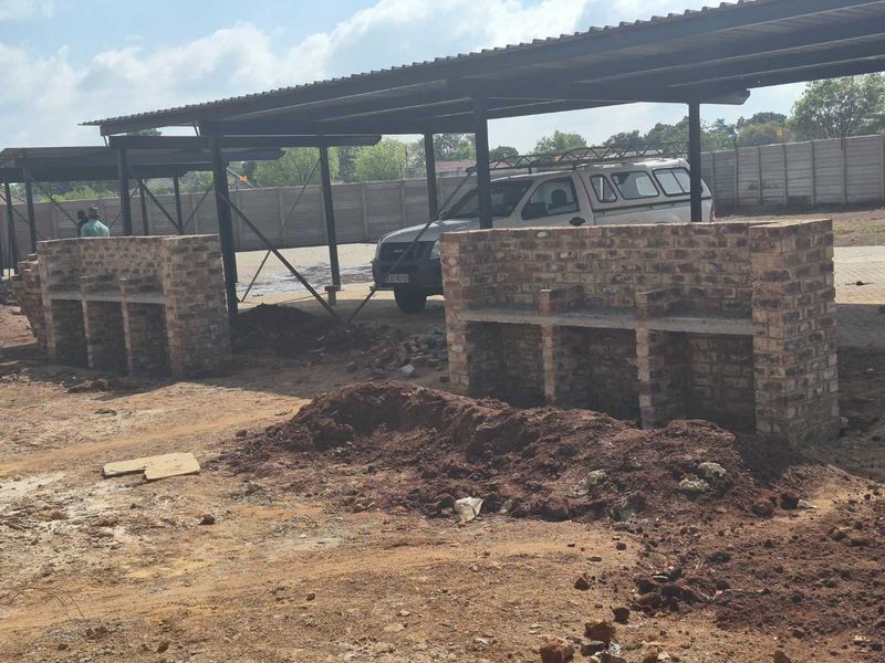 Outdoor communal area featuring brick braai stands under a metal carport structure, currently undergoing landscaping and site development.