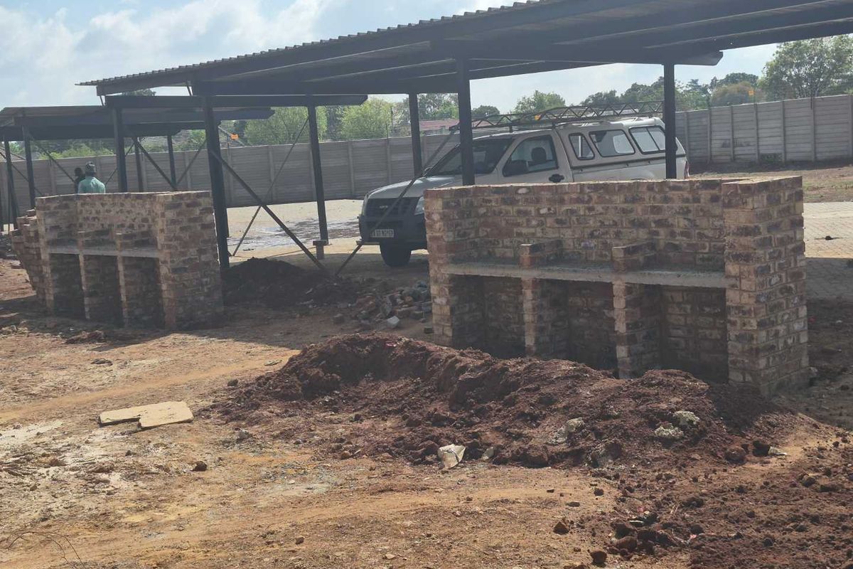 Outdoor communal area featuring brick braai stands under a metal carport structure, currently undergoing landscaping and site development.
