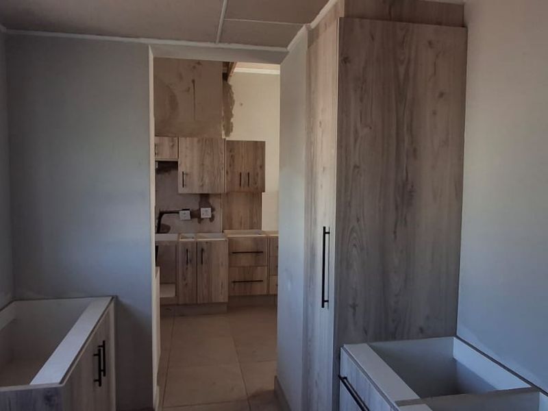 An unfinished kitchen area featuring light wood-look cabinetry and tiled flooring, currently undergoing renovation with exposed wall surfaces.