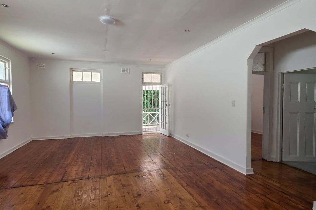 Spacious living area featuring original timber flooring, classic archway detailing, and direct access to an outdoor balcony through a traditional french door.