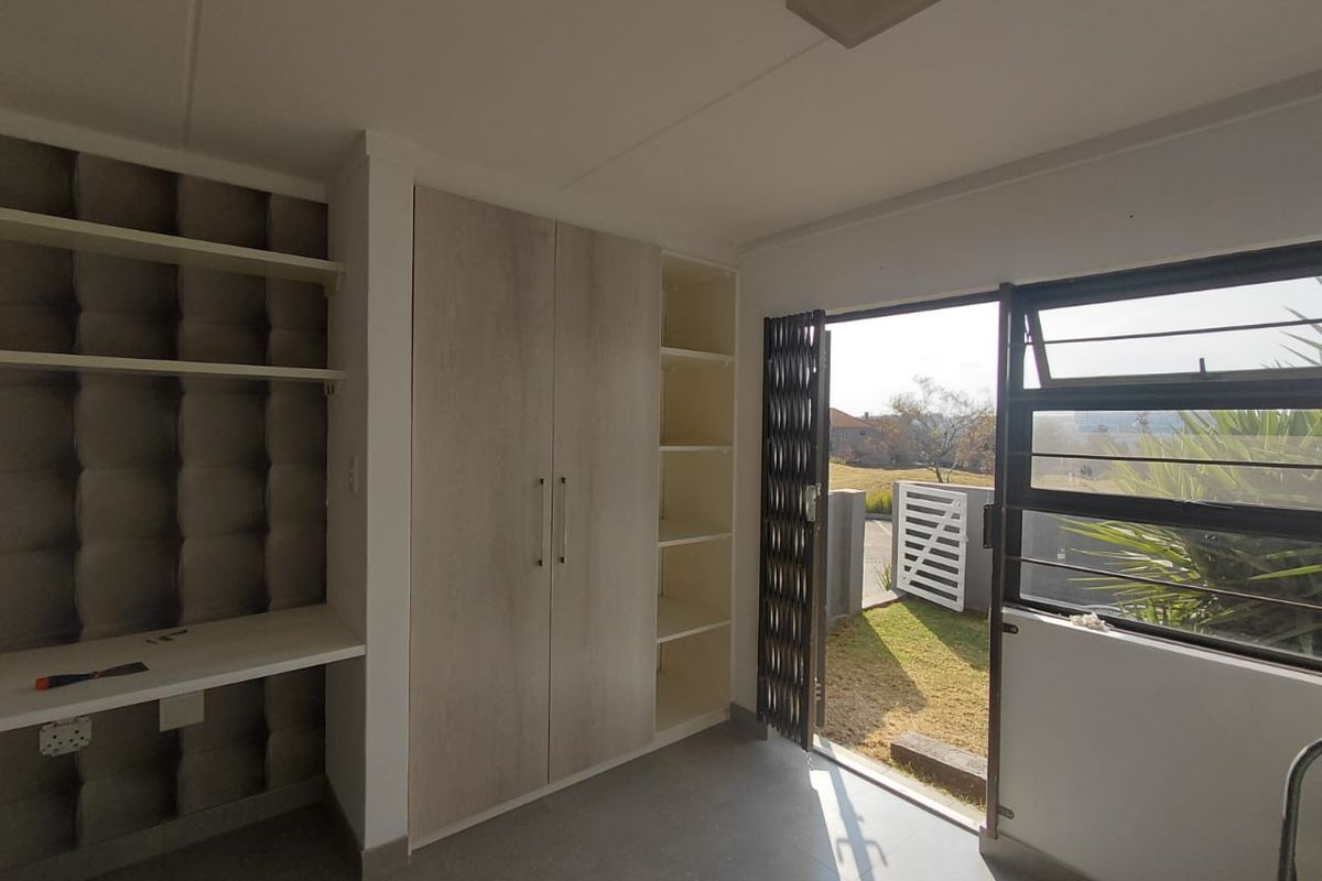 A bright bedroom featuring built-in cupboards, integrated shelving, a built-in desk, and direct access to the exterior through a security gate.