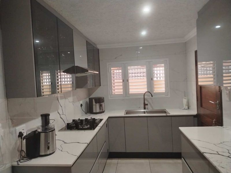 Modern kitchen featuring sleek grey cabinetry, white marble-effect stone countertops, gas hob, extractor fan, and a double sink with a contemporary mixer tap.