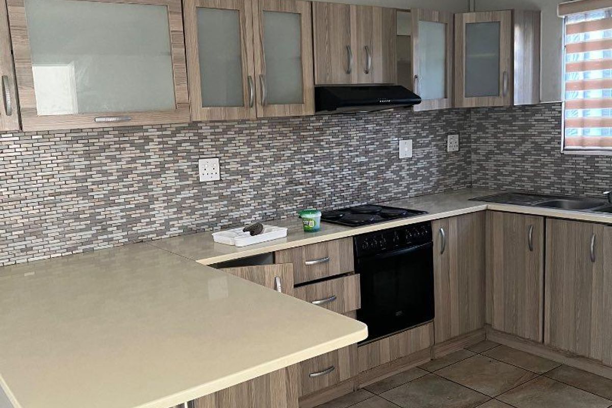 A functional kitchen featuring wood-look cabinetry, a mosaic tile backsplash, built-in oven with hob, extractor fan, and an integrated breakfast bar.