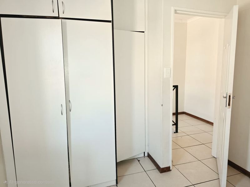 A vacant bedroom featuring built-in cupboards and tiled flooring, leading into an adjacent room through an open doorway.