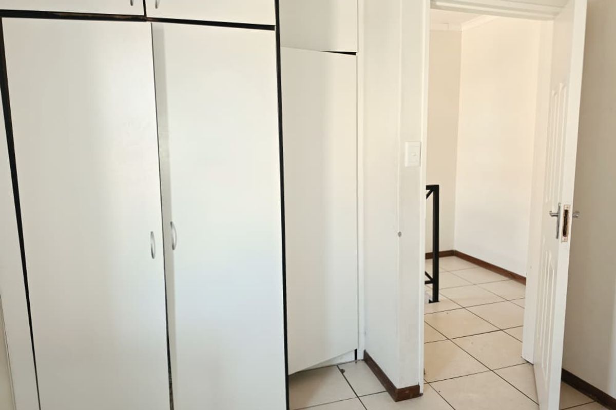 A vacant bedroom featuring built-in cupboards and tiled flooring, leading into an adjacent room through an open doorway.