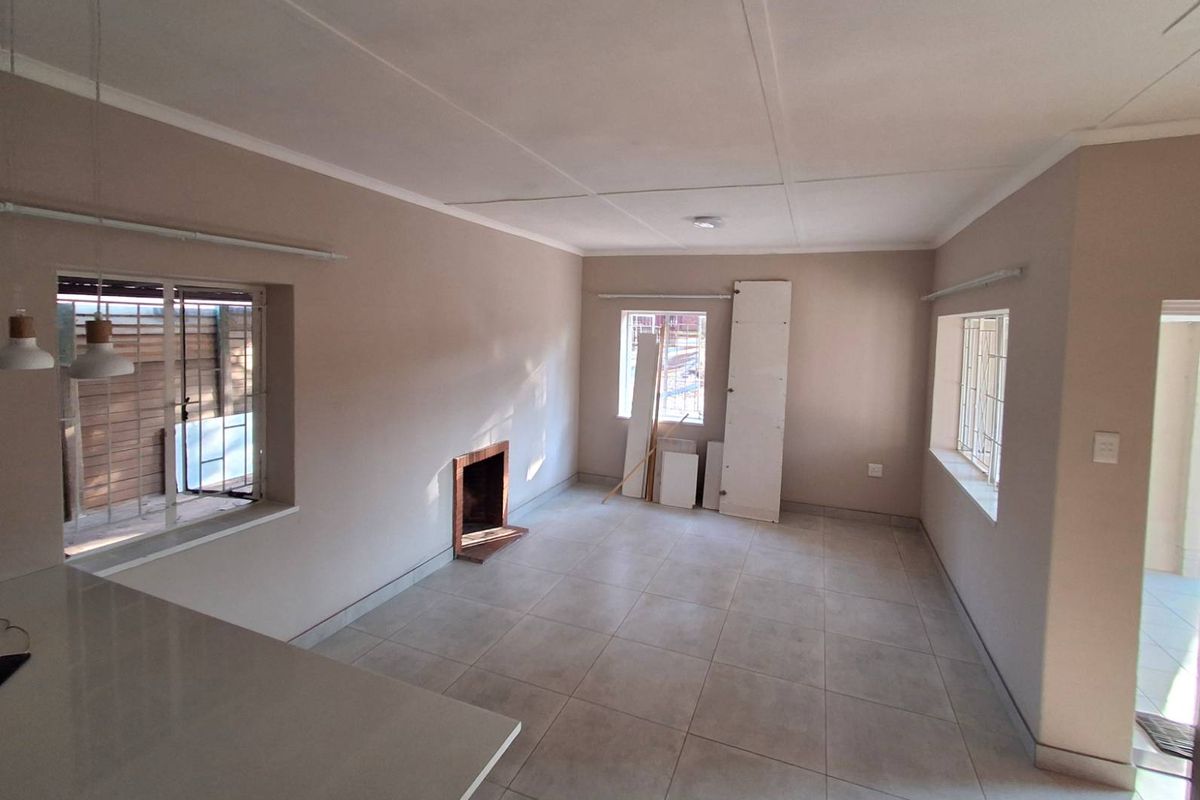 An empty, neutrally painted living room featuring tiled flooring, a built-in fireplace, and windows fitted with security bars.
