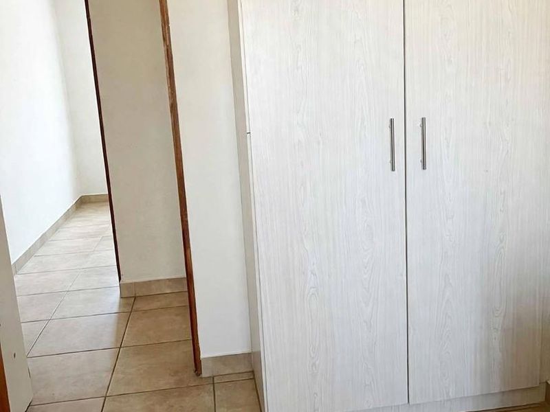 A clean, empty bedroom featuring neutral tiled flooring and a built-in wardrobe with light wood-grain finish.