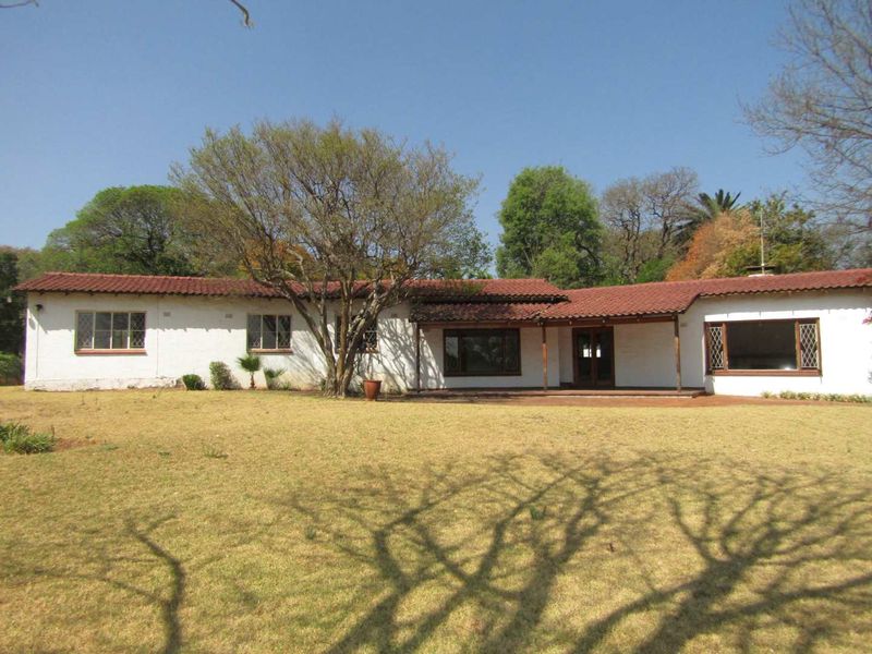 Rear view of a single-story residence featuring a covered patio, terracotta tiled roof, and expansive garden area.