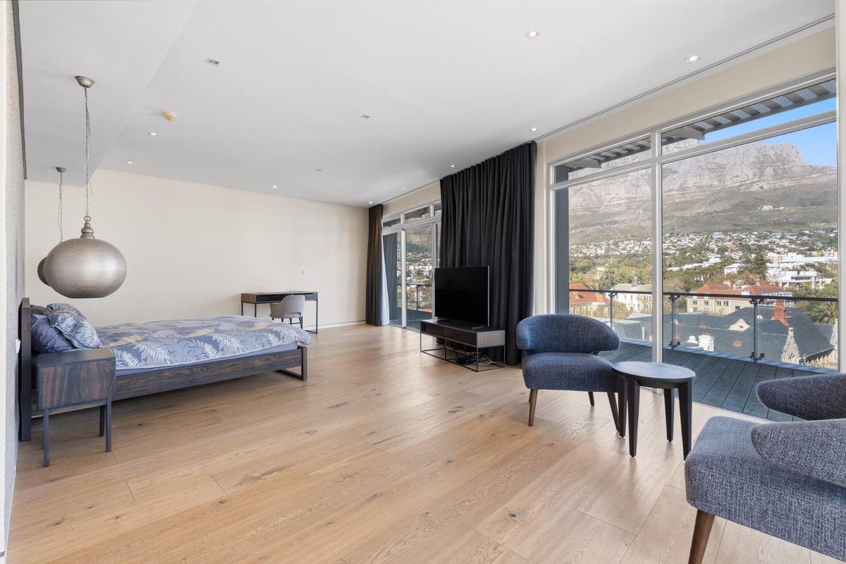 Spacious bedroom featuring light timber flooring, recessed lighting, and expansive floor-to-ceiling glass doors opening to a balcony with mountain and city views.